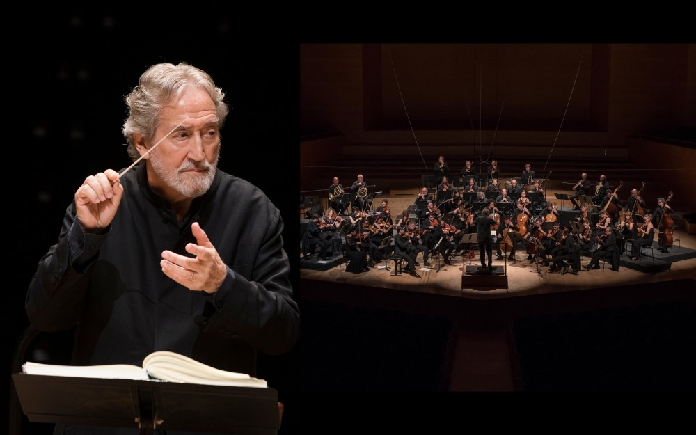 Jordi Savall gesturing beside a full symphony orchestra on stage