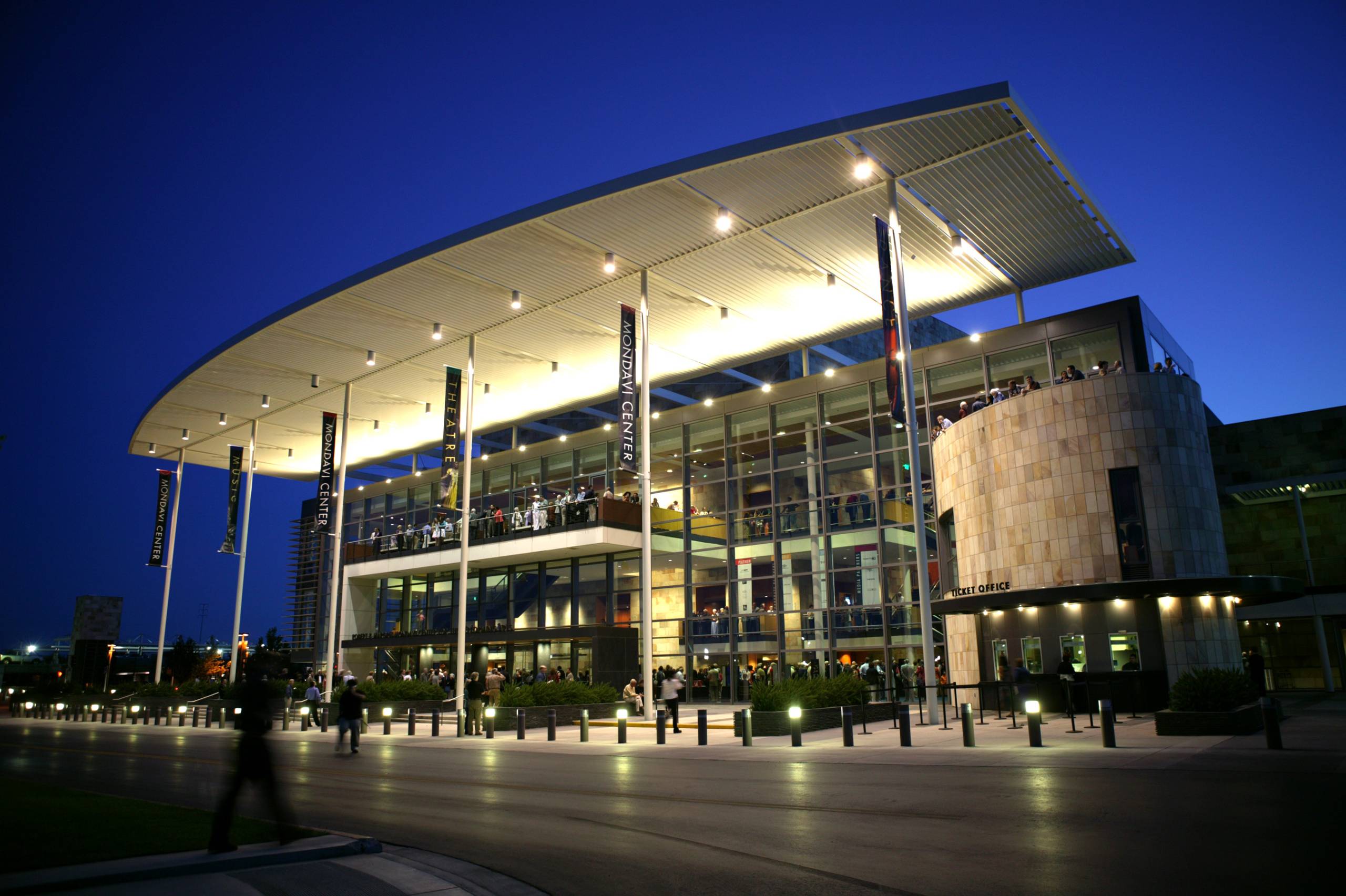 Modern building with a curved roof, illuminated at night, surrounded by landscaped pathways.