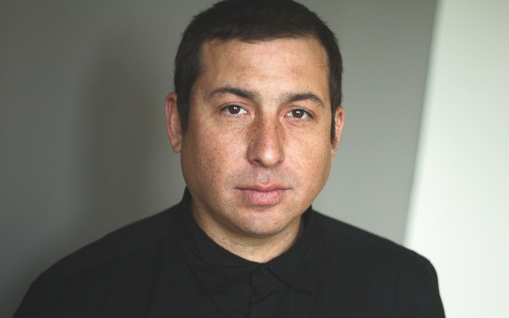 Headshot portrait of Tommy Orange with short dark hair, neutral expression, wearing dark shirt.