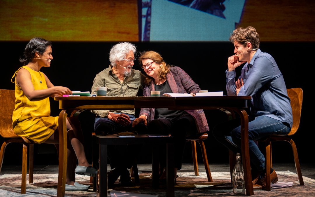 Four actors engaged in a dramatic scene around a wooden table, conveying various emotions.