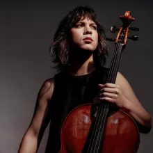 Andrew Yee holding a cello against a dark background.