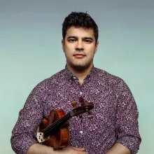 Domenic Salerni holding a violin, wearing a patterned shirt, with a blue gradient background.