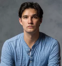 Young man headshot, neutral expression, blue henley shirt against gray textured backdrop