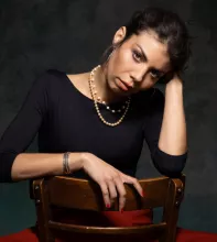Melissa Aldana sitting on a chair, with her head resting on her hand, looking pensive.