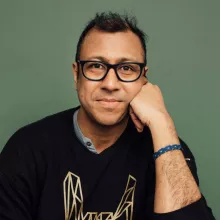 Ravi Jain with glasses and a thoughtful expression, resting his chin on his hand, against a green background.