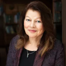 Tara Cullis with long, wavy brown hair smiles warmly, wearing a dark jacket with a subtle pattern.