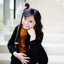 Teng Li in black seated on bright stairwell, holding violin
