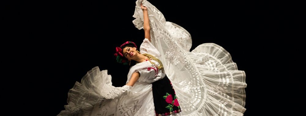 Dancer in white lace dress fanning wide skirt, holding red flowers on black background