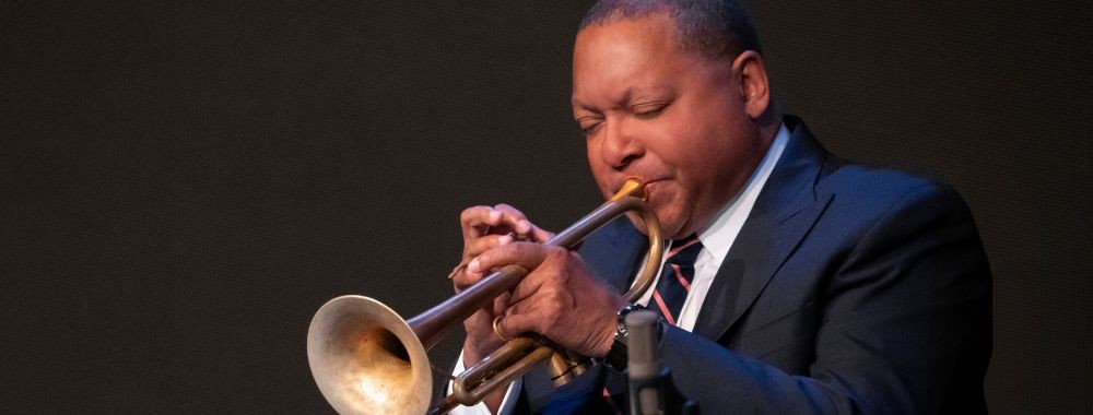 Wynton Marsalis in a suit passionately playing trumpet on dark stage