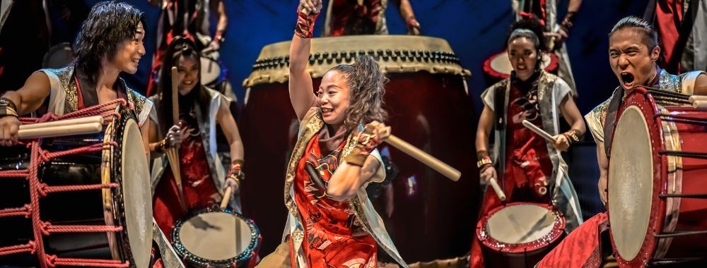 Taiko drummers in red costumes striking large drums on stage