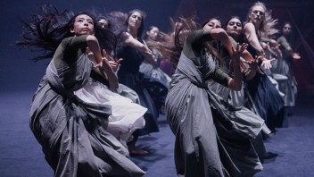 Dancers in flowing gray and white dresses in dynamic contemporary performance on dim stage