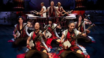 Nine Yamato performs in red-gold costumes playing taiko drums and stringed instruments.