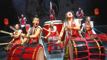 Energetic taiko drummers in red costumes playing large drums on stage