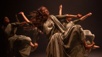 Akram Khan dancers in flowing gray dresses, hair airborne under warm stage lighting