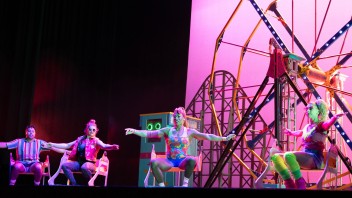 Cirque Mechanics performers in neon costumes on an amusement park set backlit by pink