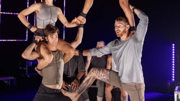 Acrobats performing a human pyramid on stage against a dark backdrop.
