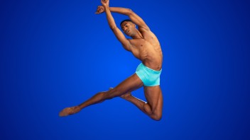Male dancer leaping  with arms above head in turquoise briefs against vivid blue background