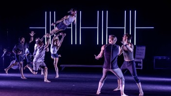 A group of dancers performing an acrobatic lift under dramatic stage lighting.