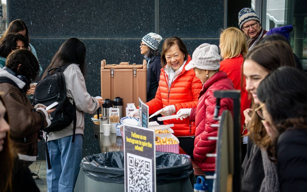 A diverse group of people gathered at a table with food, engaged in conversation outdoors.