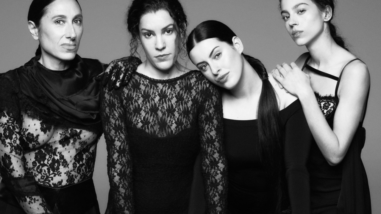 Black-and-white photo of Las Migas in elegant black dresses, posing with serious expressions
