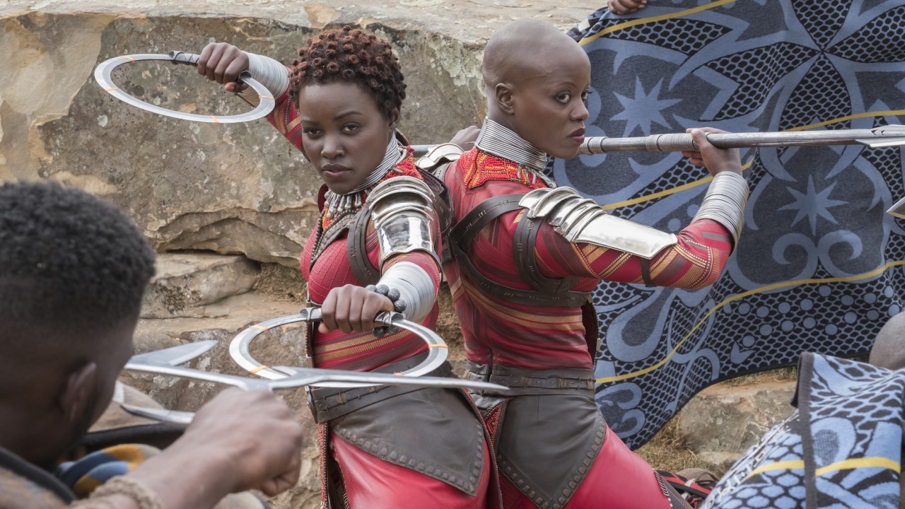 Two actors in red armor wield circular ring blades, poised against attackers