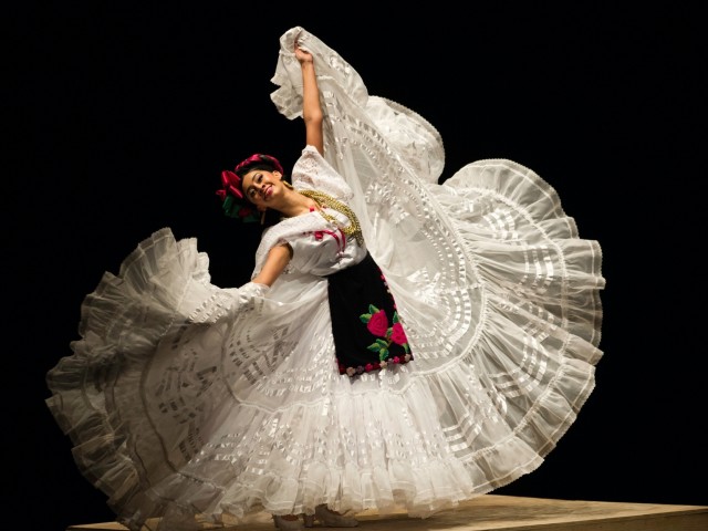 Mexican folkloric dancer in white ruffled skirt mid-twirl, embroidered bodice and red headpiece