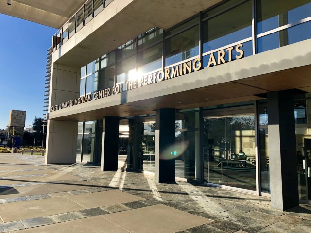 Modern building entrance with large glass doors, featuring "Performing Arts" signage.