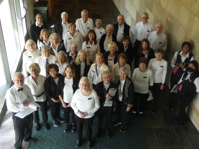 Group of seniors in black and white attire gathered indoors, smiling at the camera.