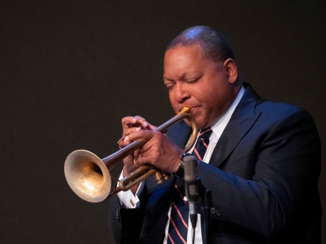 Wynton Marsalis wearing a suit and tie while playing the trumpet.