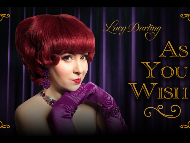 Vintage poster of coy red-haired woman in purple gloves before a purple velvet curtain with the text "Lucy Darling As You Wish" overlaid on top.