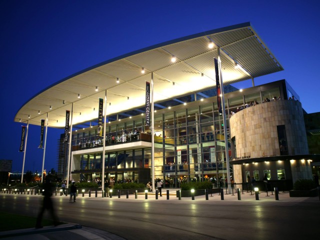 Modern building with a curved roof, illuminated at night, surrounded by landscaped pathways.