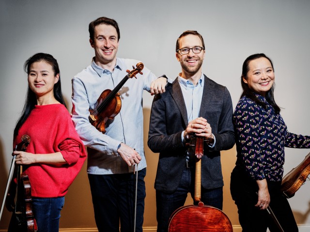 Four smiling string musicians in studio holding violins and a cello