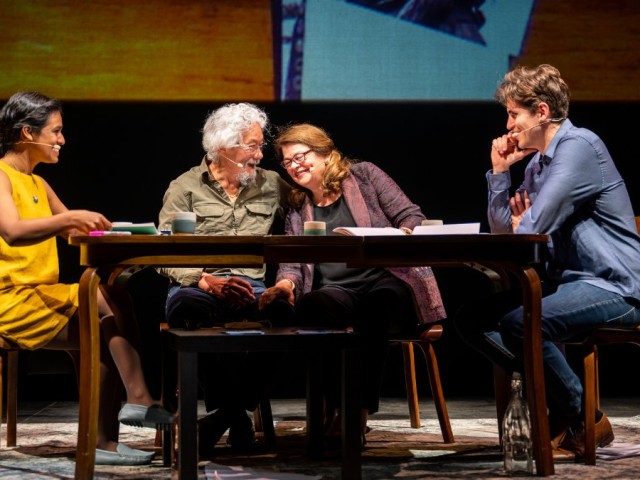 Four actors engaged in a dramatic scene around a wooden table, conveying various emotions.