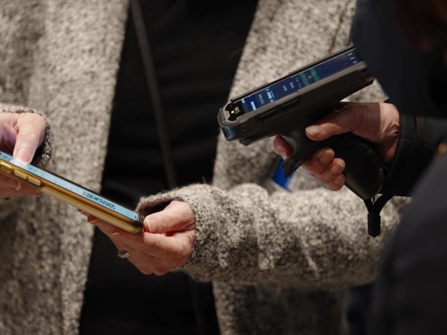 A person holding a tablet while another uses a scanning device.