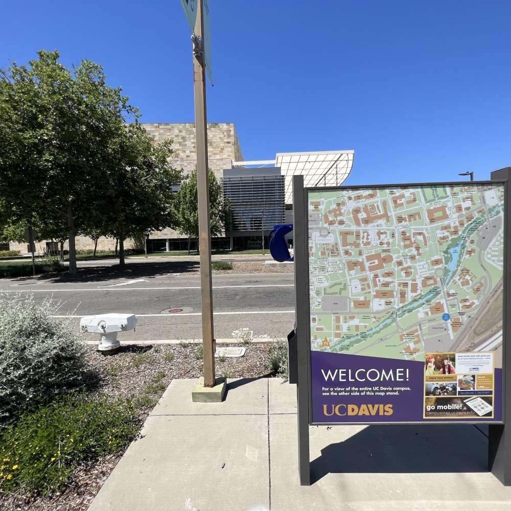 Sign displaying a campus map of UC Davis, with trees and buildings in the background.