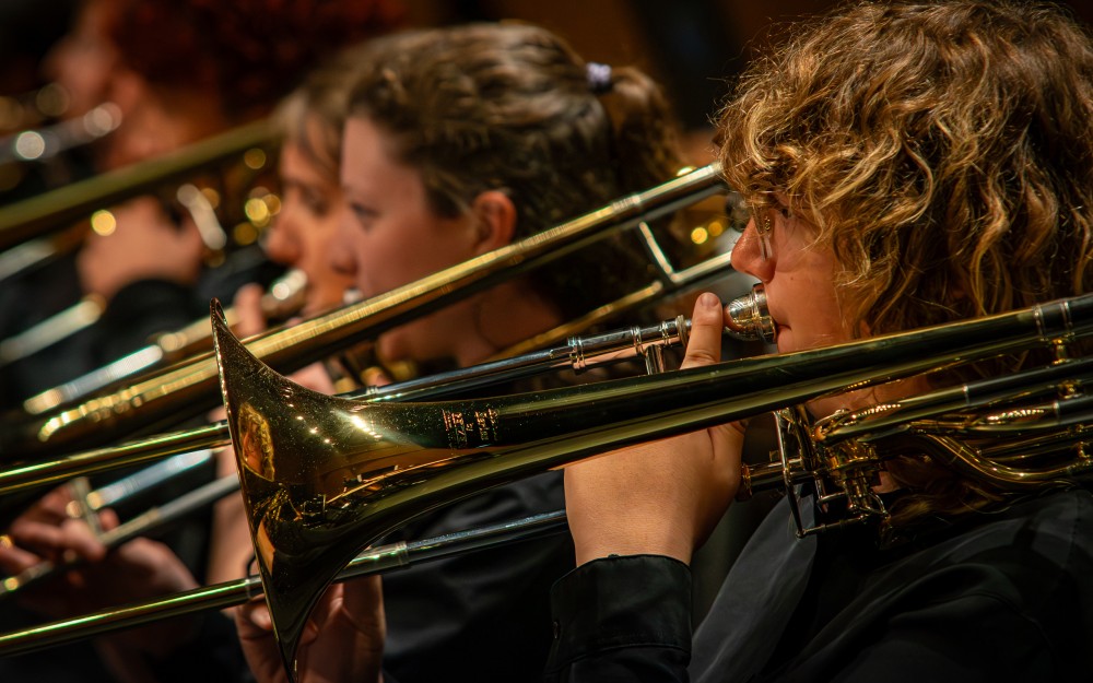 Close-up photograph of trombone players playing gleaming brass instruments