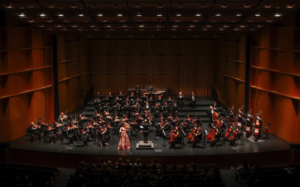 Orchestra with conductor and soloist in pink on a wood-paneled concert stage