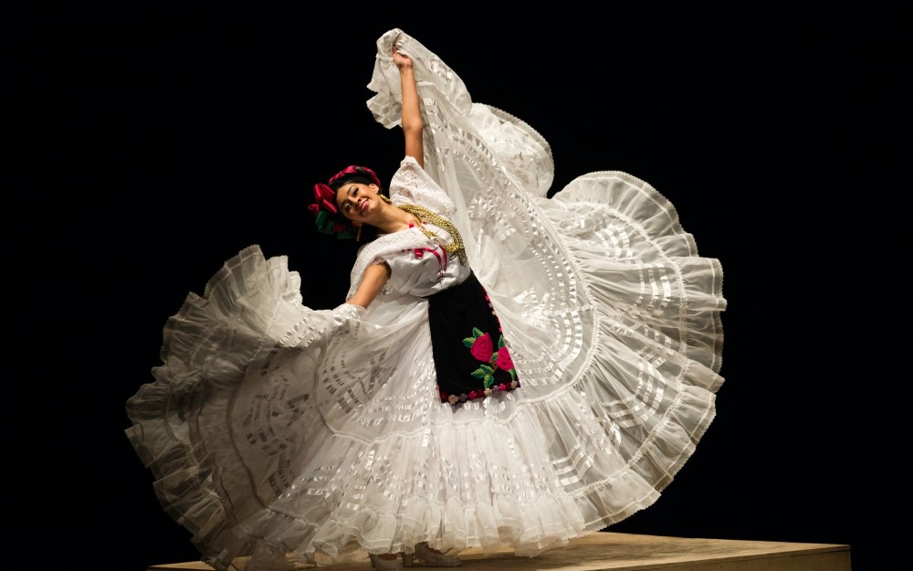 Mexican folkloric dancer in white ruffled skirt mid-twirl, embroidered bodice and red headpiece