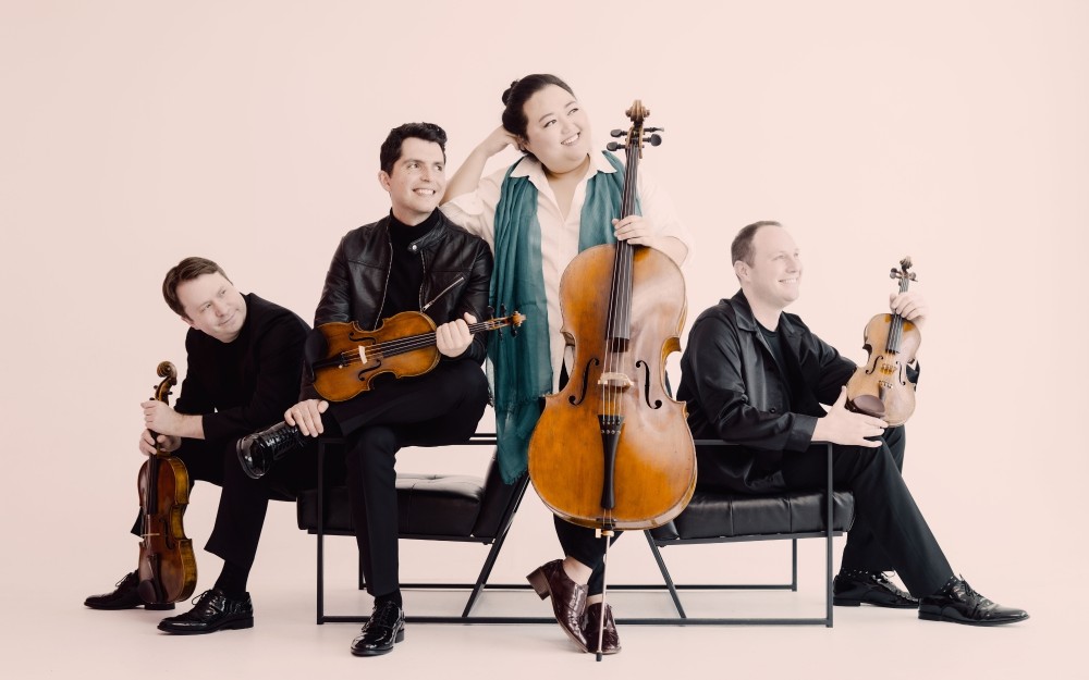 Calidore String Quartet seated with violins and a cello against a pale pink background