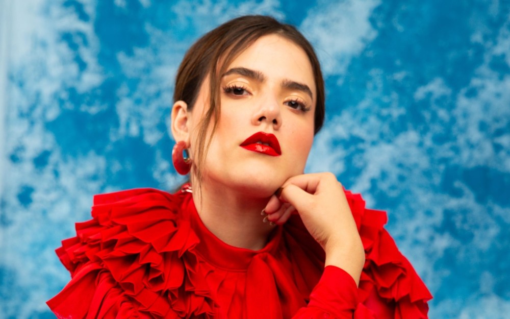 Camila Fernández posed with hand on chin, red ruffled blouse, and a blue backdrop.