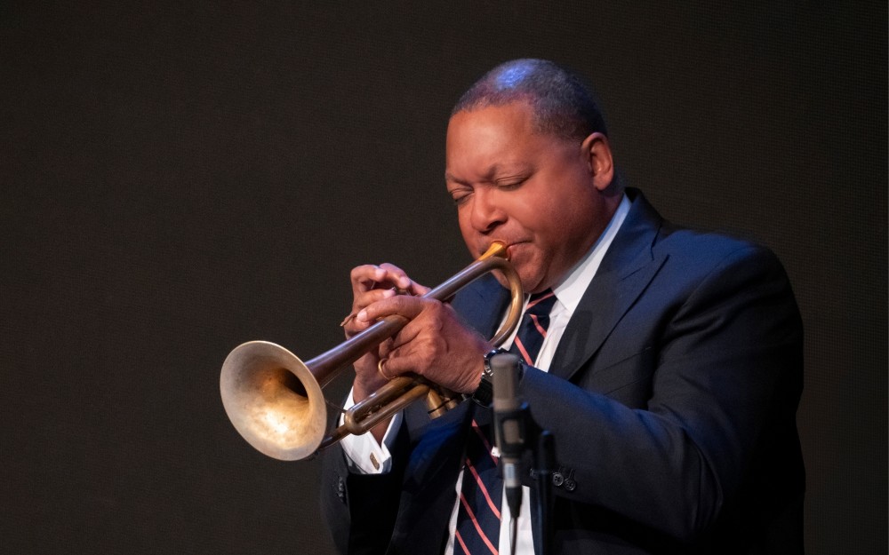 Wynton Marsalis wearing a suit and tie while playing the trumpet.