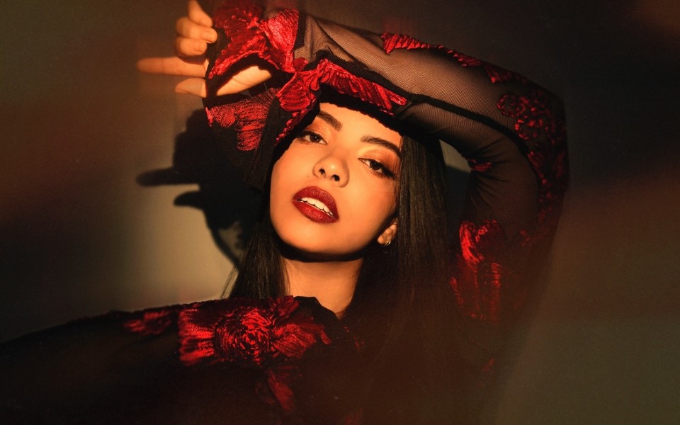 Lucía in a black dress with red accents poses confidently, with dramatic lighting.