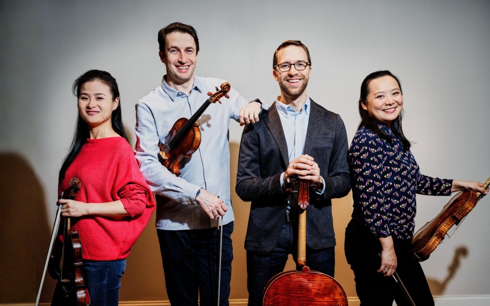 Four smiling string musicians in studio holding violins and a cello
