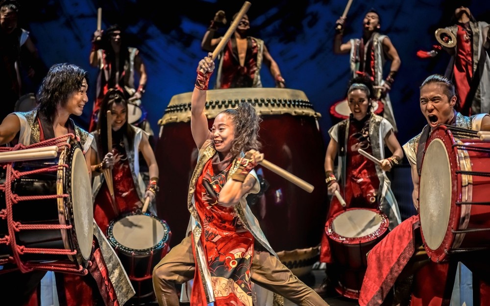 Energetic taiko drummers in red costumes performing with large drums on stage.