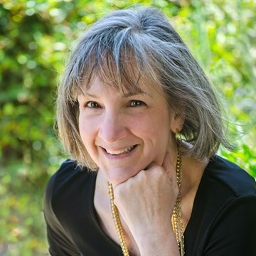 Smiling gray‑haired woman, chin resting on hand, blurred green garden background