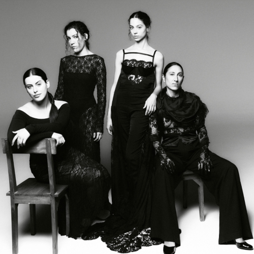 Black-and-white studio portrait of Las Migas in elegant black gowns, two seated, two standing.