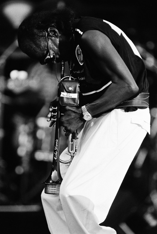 Black-and-white photo of Miles Davis hunched over, playing passionately on stage