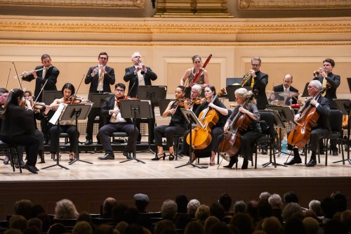 Chamber orchestra on stage in a semi-circle with an audience in a concert hall