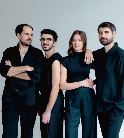 Studio portrait of four adults in coordinated black outfits against a light-gray background