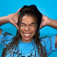 Joyful woman with braids, eyes closed and smiling against a bright blue background